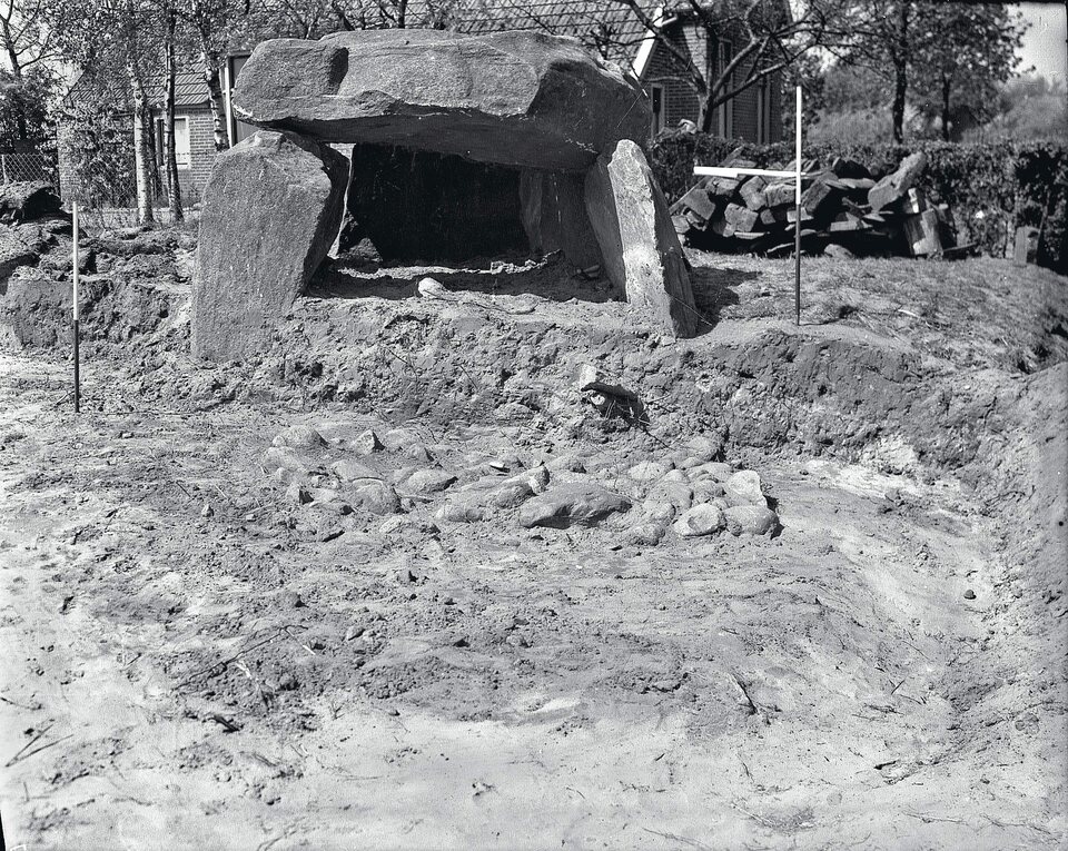 Het onderzoek van 1952, gezien vanuit het zuidoosten: de vloer van de grafkamer ligt open met de vondsten er nog op. Op de achtergrond een woning aan de Zuidlaarderweg – het hunebed lag toen al midden in het dorp.