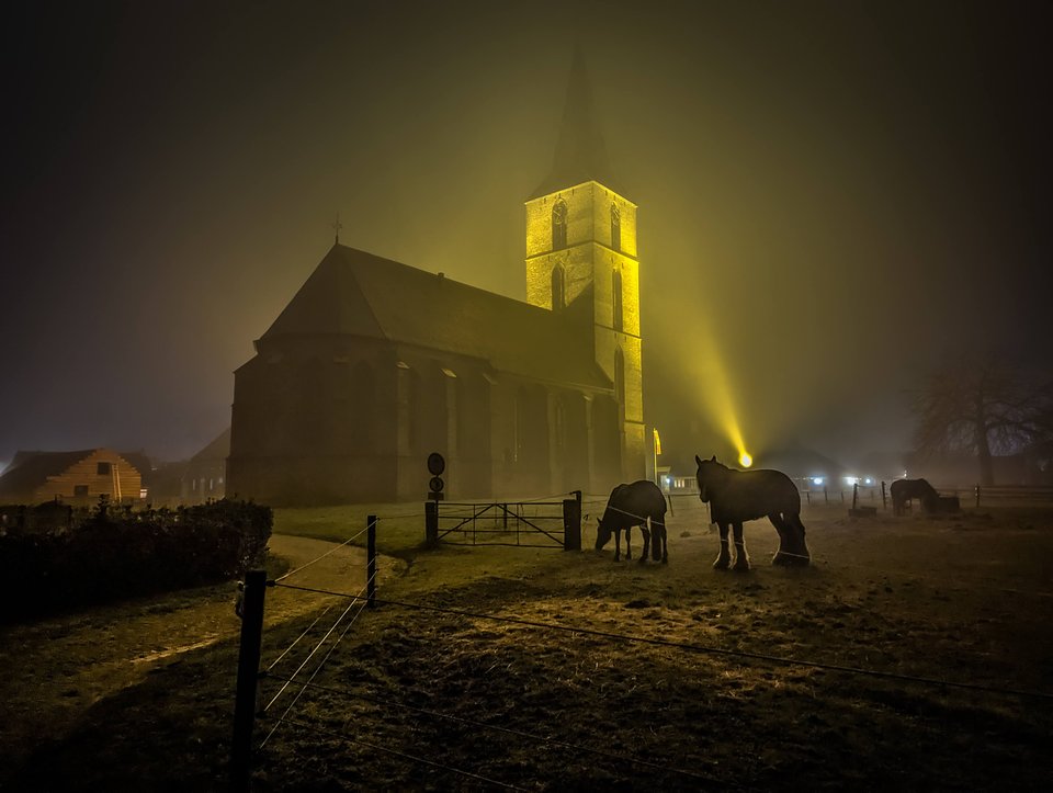 De kerk in de mist, met de toren aangelicht. Rechts de toren, links het koor – de volgorde waarin ze zijn gebouwd is de omgekeerde.
